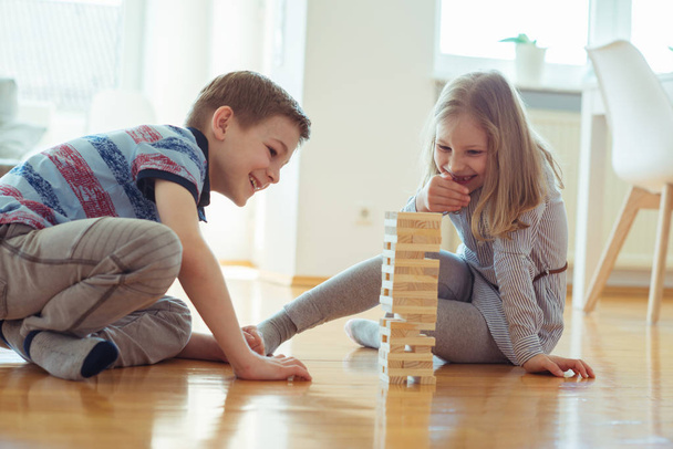 Two happy siblings playing a game with wooden blocks at home - Fotoğraf, Görsel
