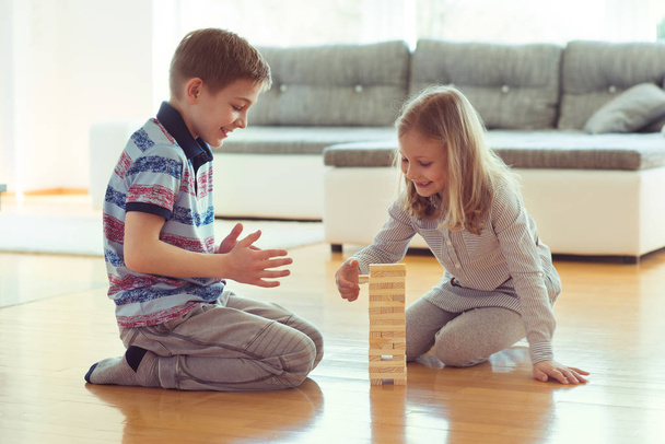 Two happy siblings playing a game with wooden blocks at home - Fotó, kép