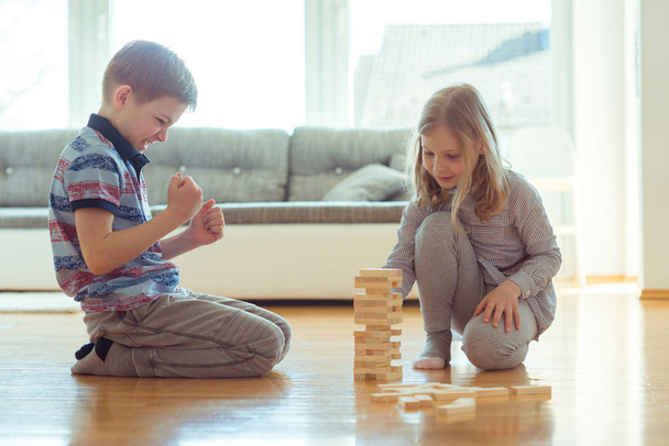 Dois irmãos felizes jogando um jogo com blocos de madeira em casa
 - Foto, Imagem