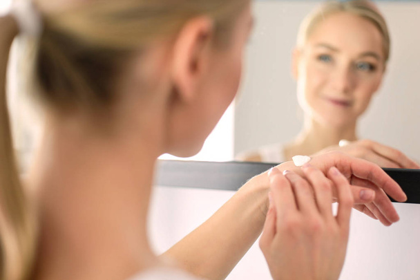 Woman caring of her beautiful skin on the face standing near mirror - 写真・画像
