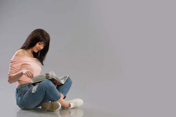 Genç kadın kat okuma kitabı gri arka plan üzerinde üzerinde rahatlatıcı - Fotoğraf, Görsel