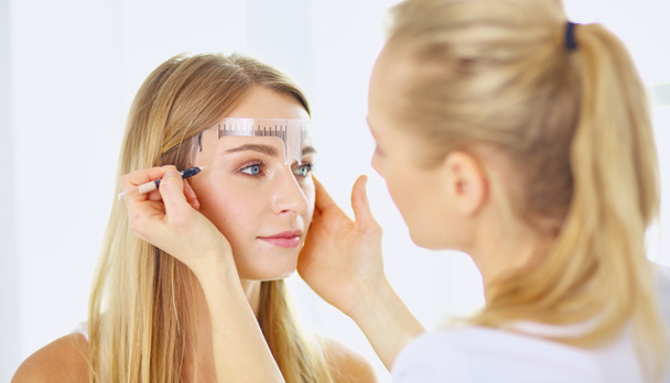 Permanentes Make-up für Augenbrauen. schöne Frau mit dicken Brauen im Schönheitssalon. Kosmetikerin tätowiert Augenbrauen für weibliches Gesicht. Schönheitsoperation - Foto, Bild
