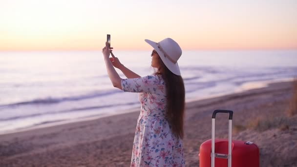 Mujer joven tomando fotos con su teléfono inteligente en la playa
 - Metraje, vídeo