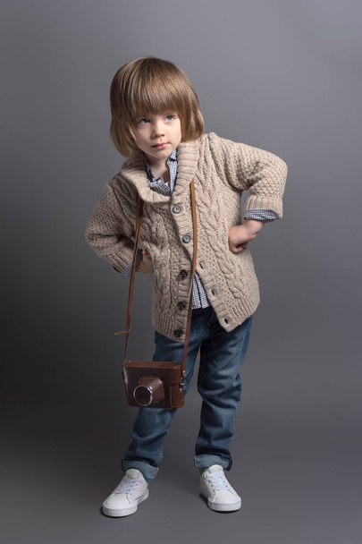 Full-length portrait of a little boy in a knitted cardigan with a vintage film camera. - Photo, image