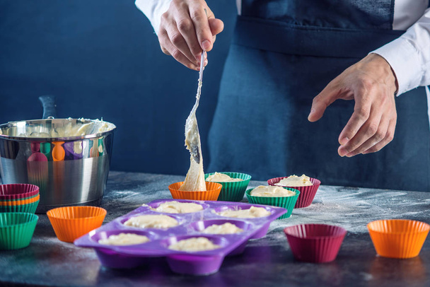 Kokki leivonnaiset musta esiliina täyttämällä taikina osaksi cupcake silikoni multaa tummalla pohjalla. Makeisten keittämisen käsite
 - Valokuva, kuva