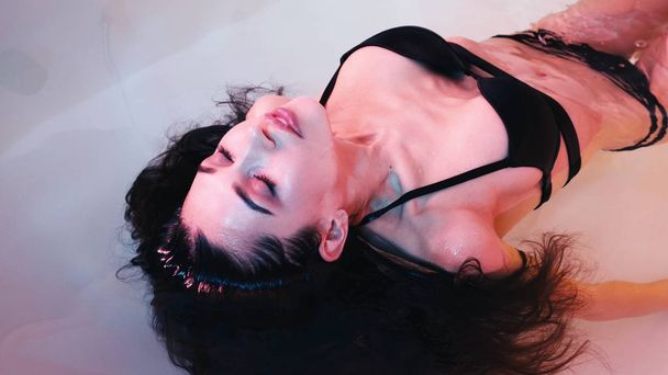 Mujer joven flotando en bañera de hidromasaje o piscina, está muy relajada. Concepto de solidez
 - Foto, Imagen