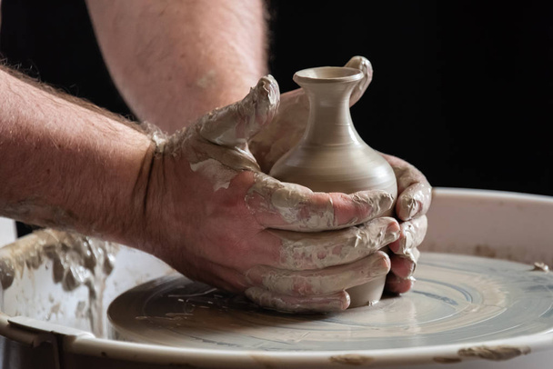 Een zeer close-up foto van de handen van een geschoolde potter gooien een pot op het wiel en afwerken van de laatste pot vloeiend maken en vormgeven van de klei - Foto, afbeelding