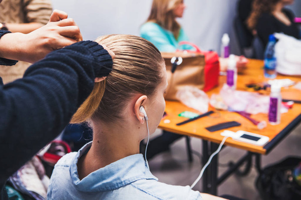 hairdresser makes a hairstyle for the blonde in the headphones in the dressing room - Photo, Image