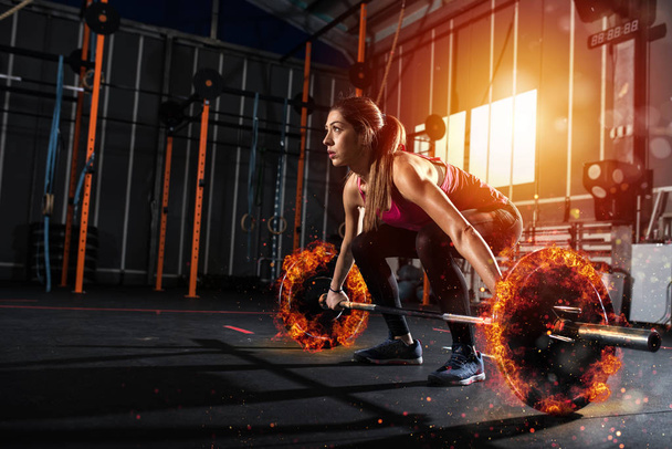 Спортивная девушка тренируется в спортзале с огненной штангой
 - Фото, изображение