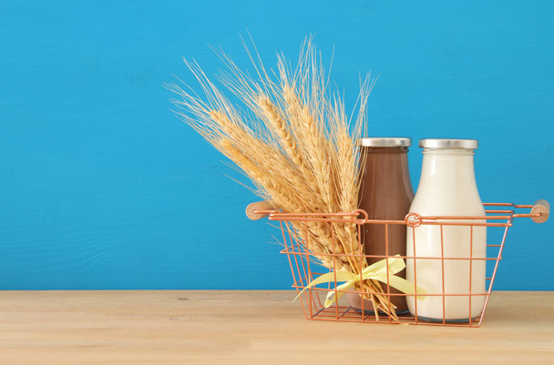 image of milk and Chocolate in the basket with wheat over wooden table and pastel background. Symbols of jewish holiday - Shavuot - Foto, Imagen