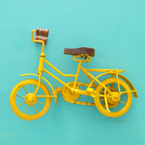 top view of vintage metal yellow bicycle toy over wooden background. - Foto, afbeelding