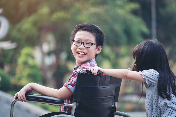 Szczęśliwy chłopiec na wózku inwalidzkim z dziewczyną spróbować jazdy wózka inwalidzkiego jej  - Zdjęcie, obraz