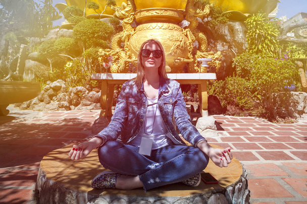 chica sentada en la posición de loto con una decoración dorada en el fondo
 - Foto, Imagen