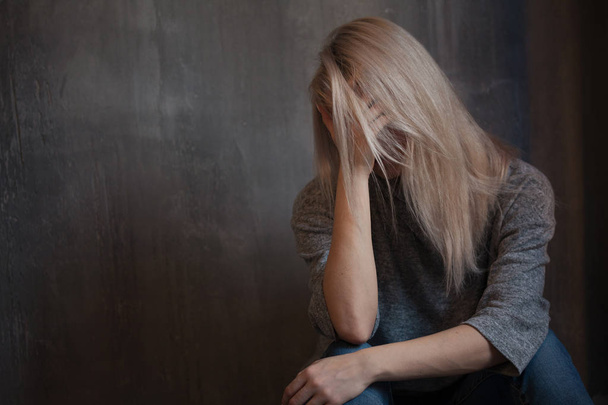 Sad young woman sitting at the wall. The young blonde. Depression and problems - Photo, Image