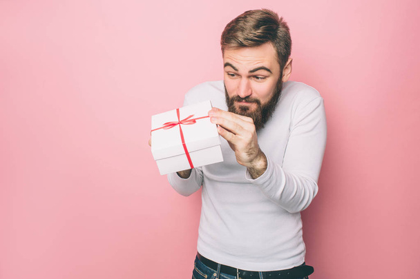 Man is holding a present in his hands. He likes it very much. Isolated on pink background. - Foto, Imagen