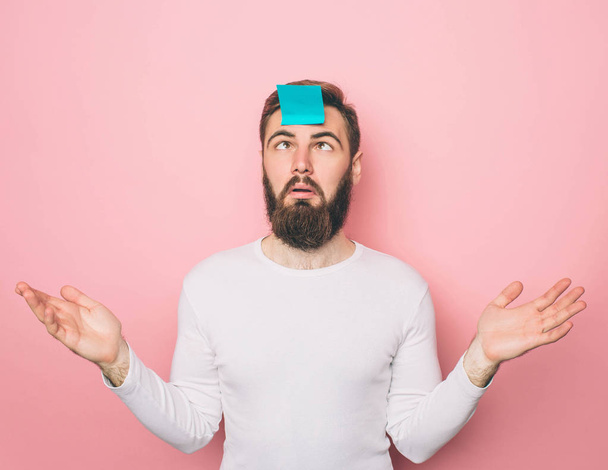 Weird guy has a blue sticker on his forehead. He is looking at it. Isolated on pink background. - Foto, Imagen