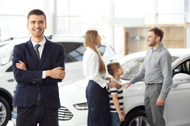 Salesman and young family in car salon - Foto, afbeelding
