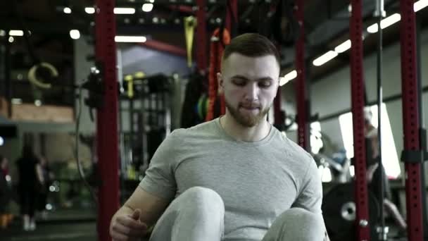 In the gym strong man does exercises on a rowing machine. - Video