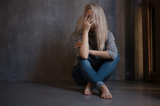 Smutny młoda kobieta siedzi na ścianie. Młoda Blondynka. Depresja i problemy - Zdjęcie, obraz