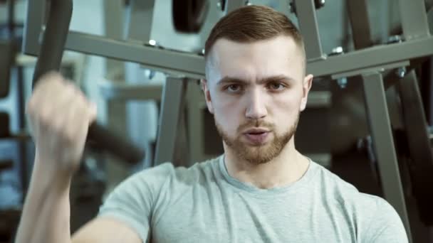 Portrait of a strong man who pulls weight with one hand on a training machine. - Video