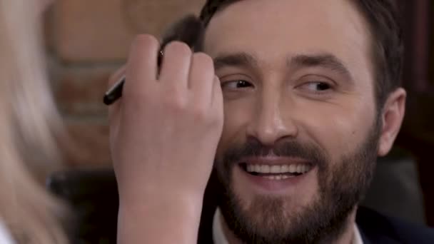 Bearded man actor is smiling while getting makeup before filming. - Video