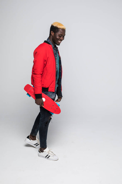 Stylish young african american skater holding longboard in hand isolated on light background - 写真・画像