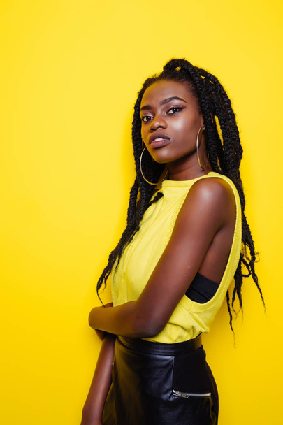 Ritratto di bellezza di giovane ragazza afroamericana in posa su sfondo giallo, guardando la fotocamera
. - Foto, immagini