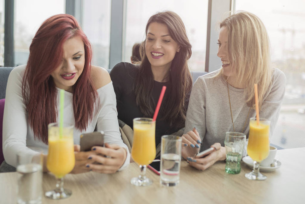 Портрет трех молодых красивых женщин, использующих мобильный телефон в ко
 - Фото, изображение