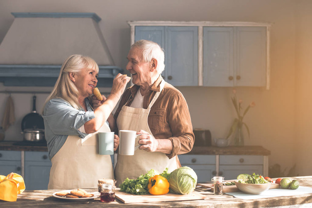 Cheerful senior couple feeding each other by sweet pastry - 写真・画像