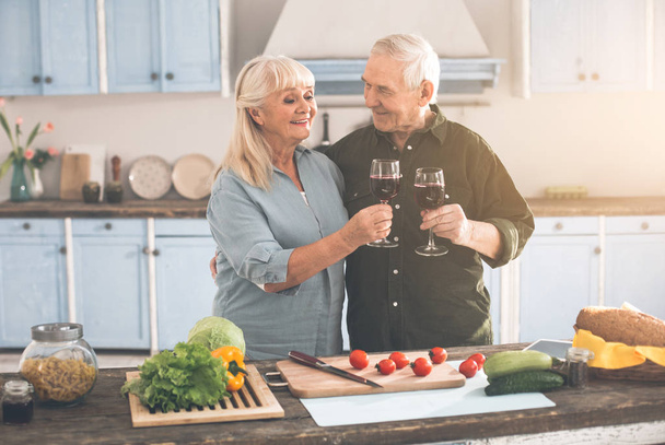 Happy old married couple drinking wine in cook room - Photo, Image