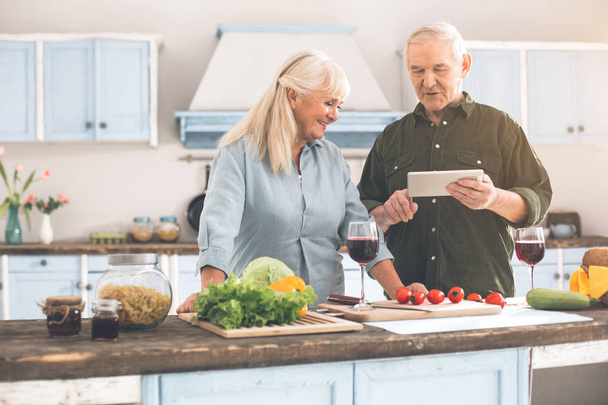 Happy senior man and woman choosing recipe on modern device - Foto, afbeelding