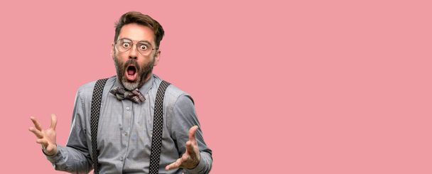 Middle age man, with beard and bow tie happy and surprised cheering expressing wow gesture - Photo, Image