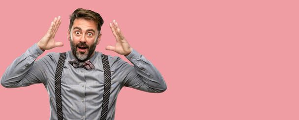 Middle age man, with beard and bow tie happy and surprised cheering expressing wow gesture - Фото, изображение