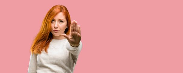 Beautiful young redhead woman annoyed with bad attitude making stop sign with hand, saying no, expressing security, defense or restriction, maybe pushing - Foto, imagen