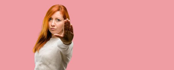 Beautiful young redhead woman annoyed with bad attitude making stop sign with hand, saying no, expressing security, defense or restriction, maybe pushing - Фото, зображення