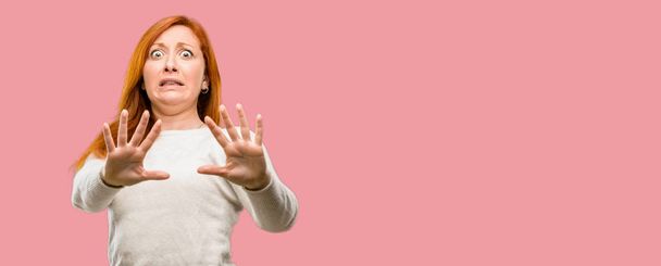 Mooie jonge roodharige vrouw walgen en boos, houden handen in stop gebaar, als een verdediging, schreeuwen - Foto, afbeelding