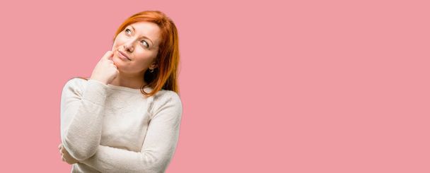 Piękna młoda redhead kobieta myśli i patrząc w górę wyrażając wątpliwości i zastanawiam się - Zdjęcie, obraz