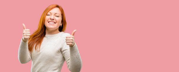 Beautiful young redhead woman smiling broadly showing thumbs up gesture to camera, expression of like and approval - Foto, imagen