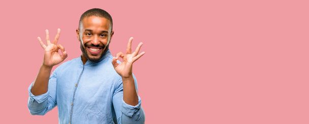 Αφρικανική αμερικανική άνδρα με μούσι κάνει εντάξει σημάδι χειρονομία με τα δύο χέρια εκφράζοντας διαλογισμού και χαλάρωσης - Φωτογραφία, εικόνα