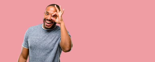 Homme afro-américain avec barbe regardant la caméra à travers les doigts dans le geste ok. Imitation de jumelles, beaux yeux et sourire
 - Photo, image