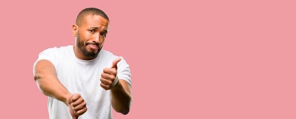 African american man with beard confused with thumbs up and down, trying to take a decision expressing doubt and frustration - Foto, Bild
