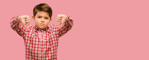 Jóképű tipegő gyermek mutatja a hüvelykujját lefelé boldogtalan jele ellenszenv, a negatív kifejezés és a helytelenítés zöld szemmel - Fotó, kép