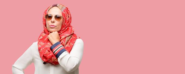 Muslimische arabische Frau mittleren Alters, die Hijab trägt und aufblickt, um Zweifel und Verwunderung auszudrücken - Foto, Bild