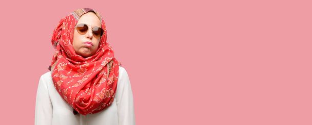 Mulher árabe muçulmana de meia idade vestindo hijab com expressão sonolenta, sendo sobrecarregado e cansado
 - Foto, Imagem