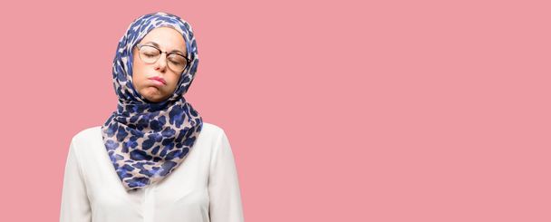 Мусульманская арабская женщина средних лет носит хиджаб со сонливым выражением лица, будучи перегруженной работой и уставшей
 - Фото, изображение