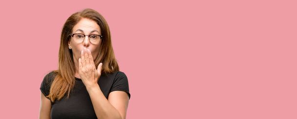 Жінка середнього віку в чорній сорочці і окулярах покриває рот шоком, виглядає сором'язливо, виражаючи тишу і помилкові концепції, наляканий
 - Фото, зображення