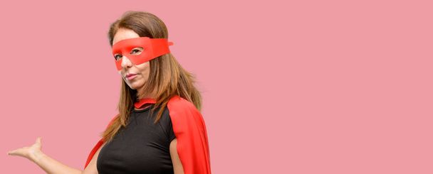 Μέσης ηλικίας γυναίκα σούπερ ήρωας φοράει κόκκινη μάσκα και Ακρωτήριο αυτοπεποίθηση και χαρούμενοι με ένα μεγάλο φυσικό χαμόγελο καλώντας να εισέλθουν - Φωτογραφία, εικόνα