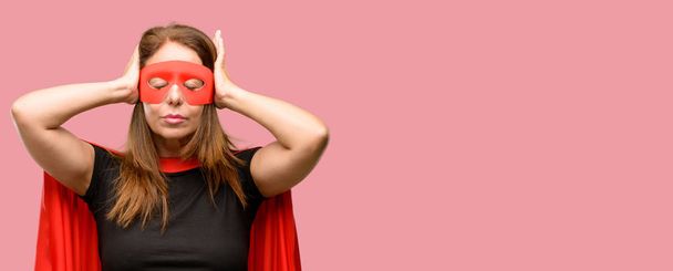 Middelbare leeftijd super held vrouw dragen rode masker en cape over oren negeren vervelend lawaai, pluggen oren om te voorkomen dat geluid van de hoorzitting. Lawaaierige muziek is een probleem. - Foto, afbeelding