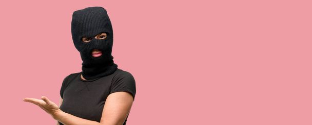 Mujer terrorista ladrón con pasamontañas de pasamontañas sosteniendo algo en la mano vacía
 - Foto, imagen
