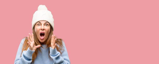 Middle age woman wearing wool winter cap stressful keeping hands on head, terrified in panic, shouting - Foto, imagen